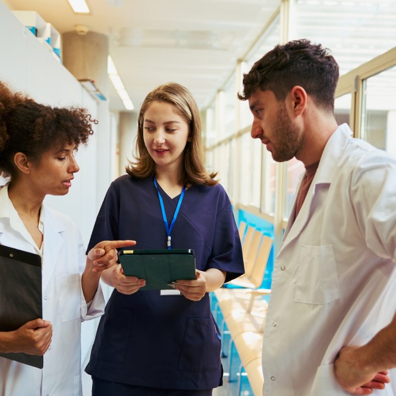 Medical team discussing patient data using tablet in hospital corridor